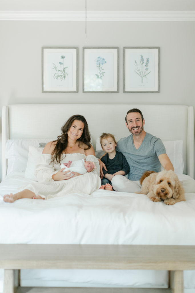 Family of 4 sitting on bed at in home newborn session
